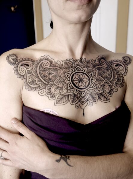Chest tattoo on a woman, tattoo has paisley designs and geometric patterns and a mandala.