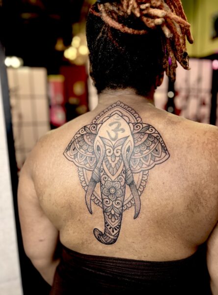 A black woman with dreadlocks and a ornamental elephant tattoo on her upper back