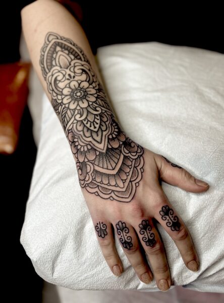 Woman's arm with ornamental flower designs and finger tattoos