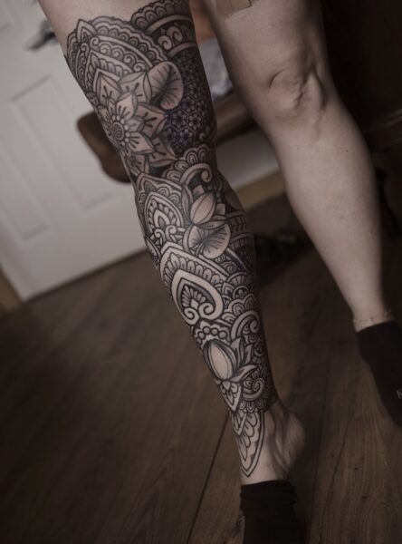 Woman with a 3/4 leg tattoo with lotus flowers and ornamental and geometric patterns