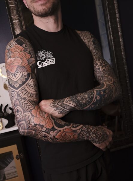 Man with two ornamental geometric sleeve tattoos with mandalas and flowers.