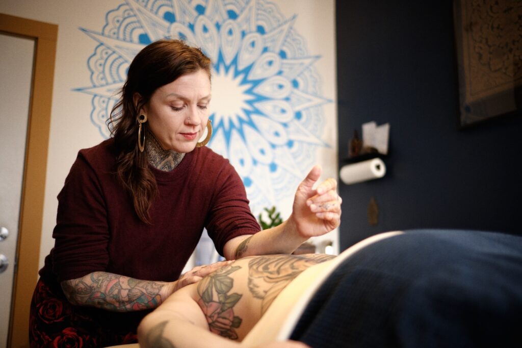 A female massage therapist giving a therapeutic massage to a client with a mandala mural on the background.